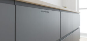 Närbild av en ljusgrå, handtagslös kökslucka med matt yta.