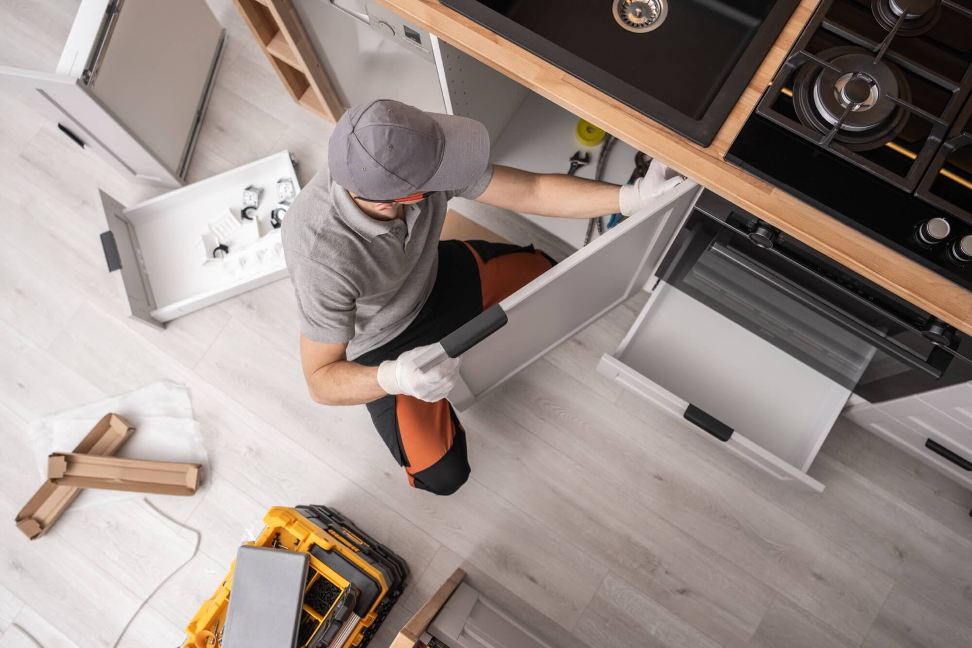 En köksinstallatör, sedd ovanifrån, justerar en skåplucka för att slutföra en köksrenovering.