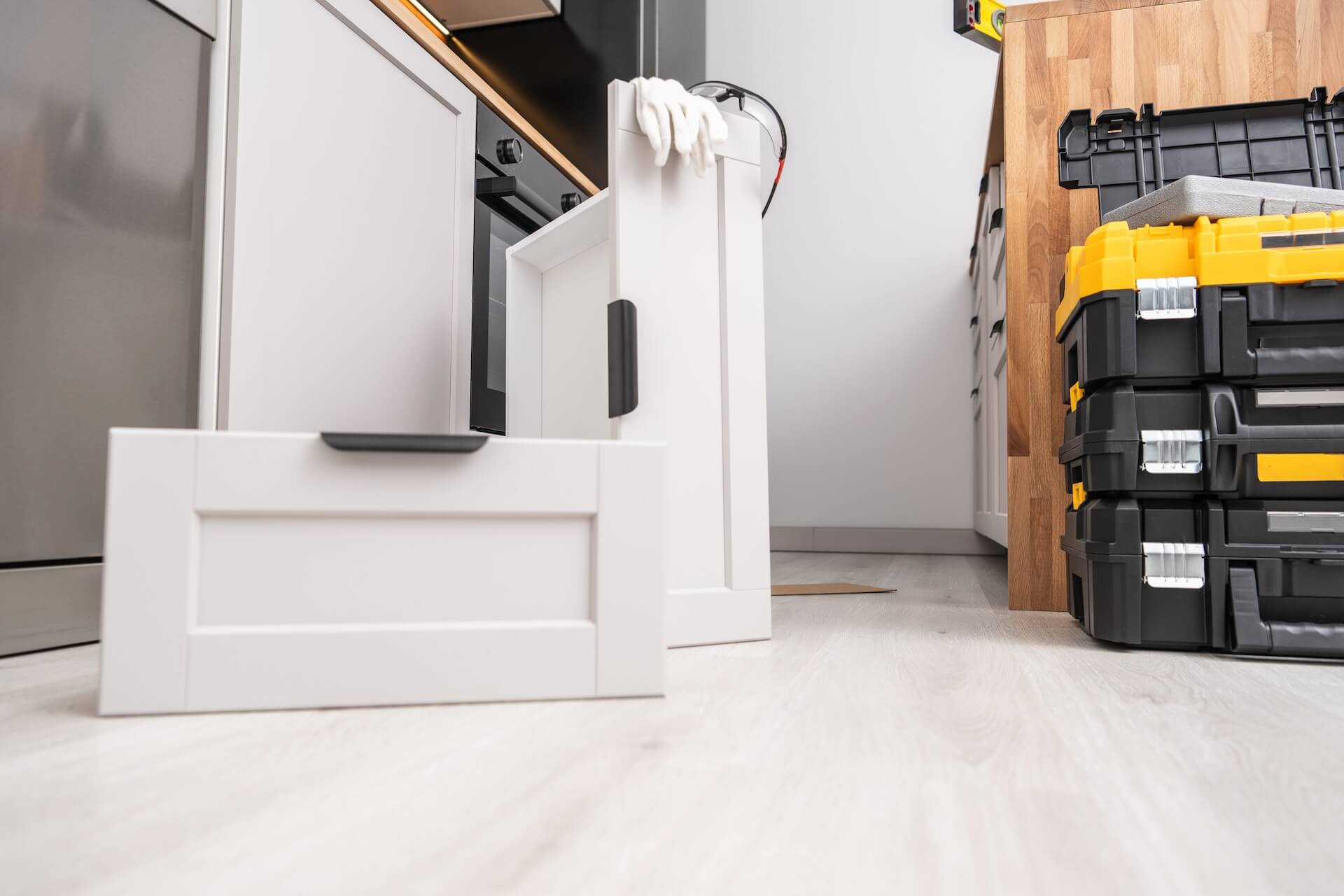 Bild från golvnivå som visar en pågående köksrenovering med verktygslådor och delar till köksskåp på golvet.
