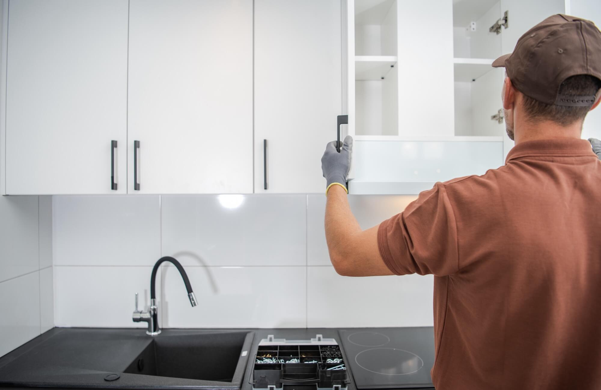 En hantverkare monterar luckan på ett överskåp, ett viktigt steg för att färdigställa en köksrenovering.