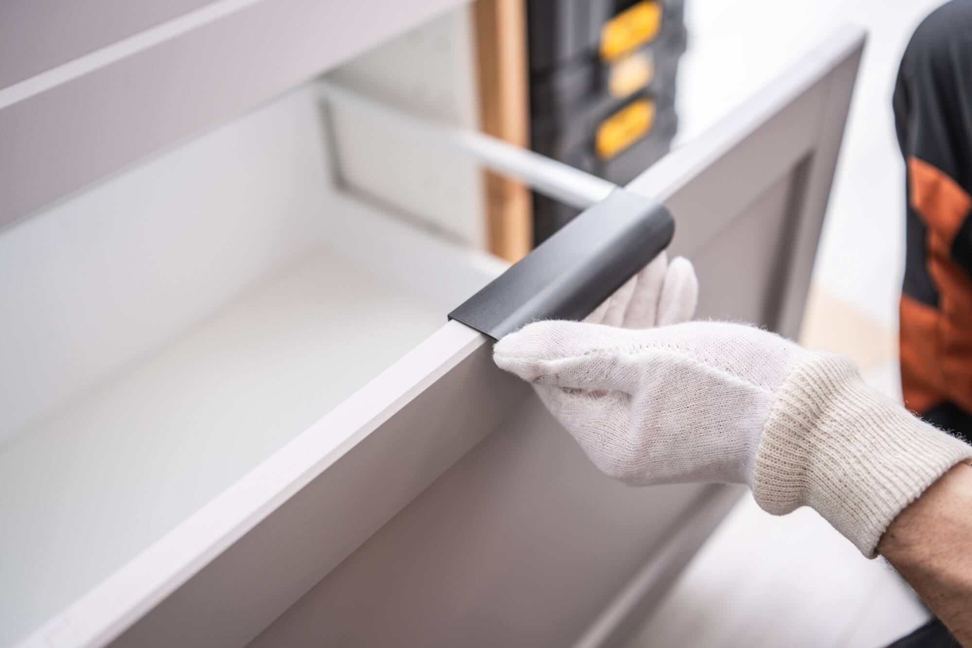 En hantverkare i vita handskar monterar ett svart handtag på en vit kökslåda under en köksrenovering.