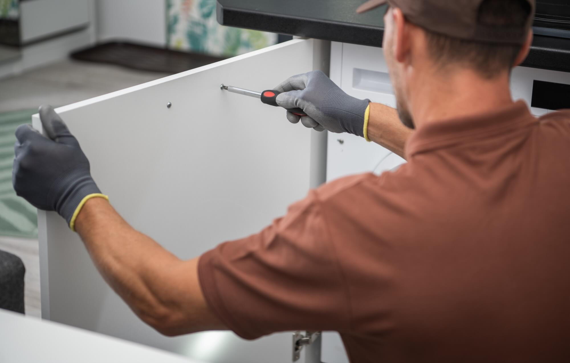 En professionell snickare skruvar fast en kökslucka, ett precisionsarbete under en köksrenovering.