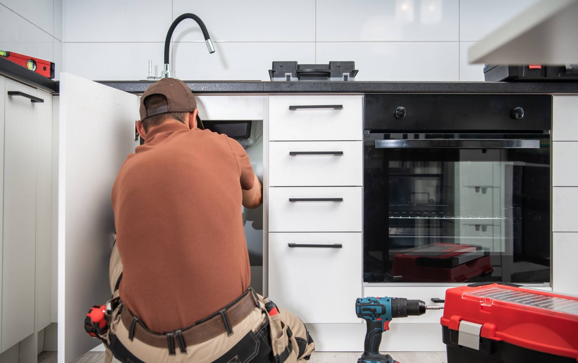 En hantverkare arbetar med VVS-installationer under diskbänken i ett modernt kök som genomgår en köksrenovering.