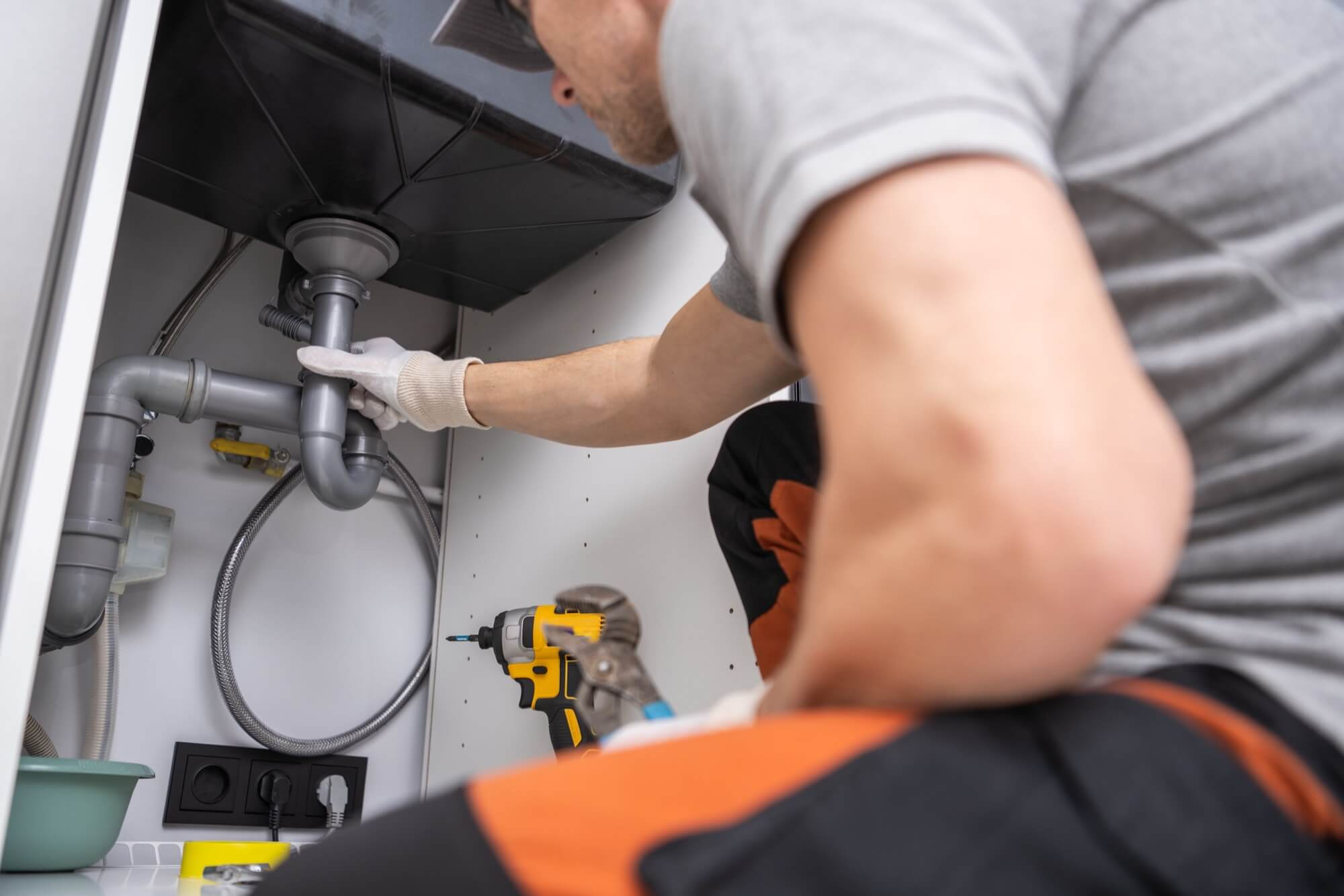 En rörmokare ansluter avloppsrören under diskbänken, ett kritiskt steg i en köksrenovering.