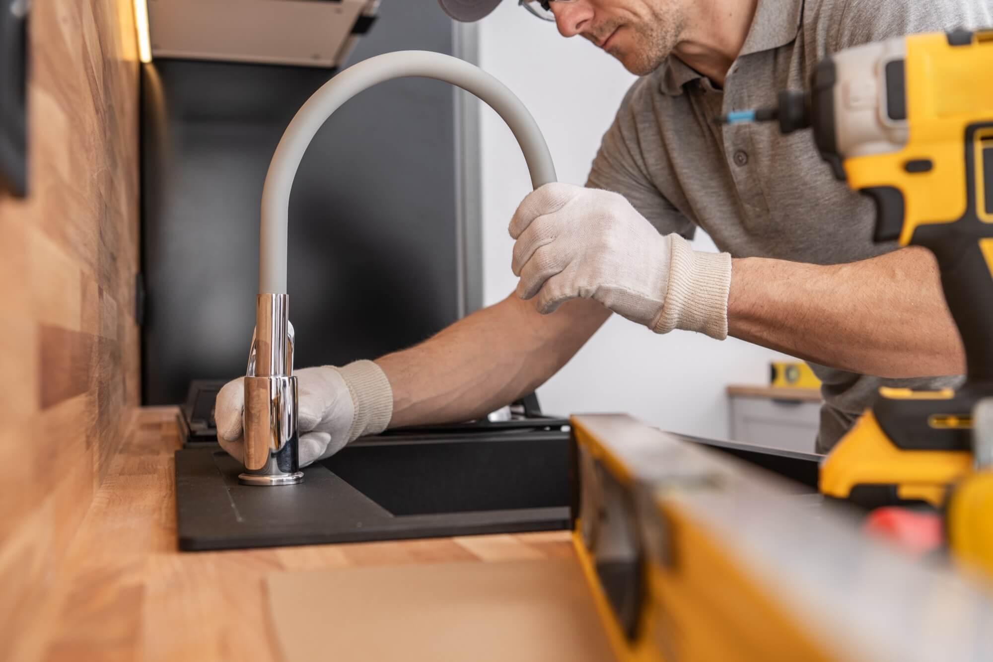 En VVS-montör installerar en ny blandare i köket, ett viktigt moment i en komplett köksrenovering.